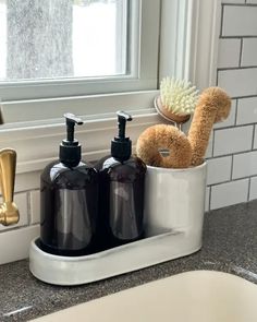 two soap dispensers and a brush in a cup on a counter next to a sink