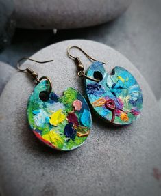 a pair of colorful earrings sitting on top of a rock next to a stone wall