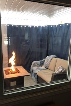 a living room with a couch and fire pit in the center, as seen through a window