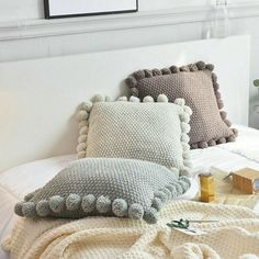 two pillows on top of a bed covered in blankets and crocheted pom - poms