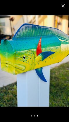 a yellow and blue fish mailbox sitting on top of a white post