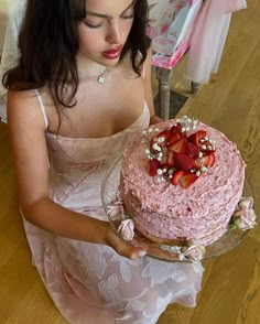 a woman in a pink dress holding a strawberry cake