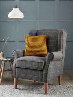 a chair with a yellow pillow on it in front of a blue wall and lamp