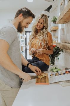 a man and woman standing in a kitchen preparing food on a cutting board next to each other