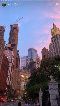 people are walking on the sidewalk in front of tall buildings under a pink and blue sky