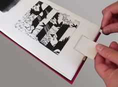 two hands are opening an open book with black and white designs on the pages,