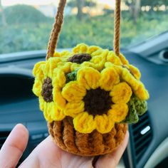 a hand holding a small crocheted sunflower purse in the dashboard of a car