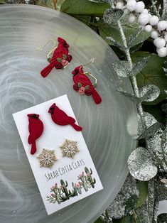 three red bird earrings sitting on top of a white plate next to some christmas decorations