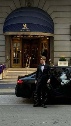 a man in a tuxedo standing next to a black car