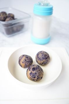 three blueberry muffins on a white plate next to a container of yogurt