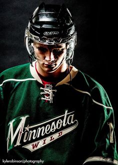 a young man wearing a green hockey uniform and holding a black helmet with the minnesota wild written on it