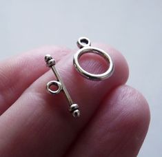 a tiny silver key shaped charm on someone's finger with the letter o in it