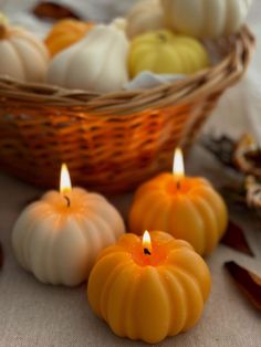 three pumpkin candles sitting on top of a table next to other small pumpkins in a basket