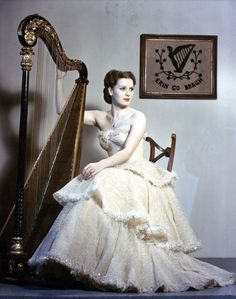 a woman in a white dress sitting on a chair next to a large wooden harp