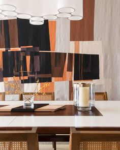 a dining room table with candles and vases on it in front of an abstract wallpaper