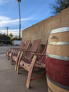 several wooden chairs lined up against a brick wall with palm trees in the back ground