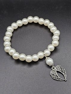 This bracelet features elegant, round white beads strung together on an elastic cord with an angel wings charm. The charm, split into two symmetrical halves, symbolizing protection and guidance. The bracelet makes a meaningful accessory suitable for any occasion. Angel Bracelet, Bead Stringing, Guardian Angel, An Angel, White Beads, Bead Bracelet, Angel Wings, Arm Band, Bracelet Making