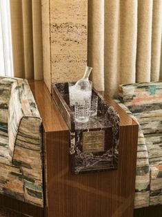 a glass sitting on top of a wooden table next to a chair and window with drapes