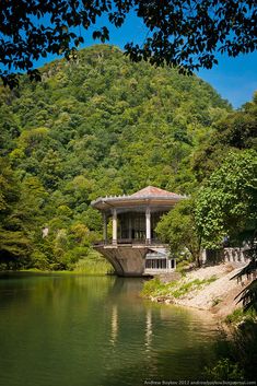 a small building sitting on top of a lush green hillside next to a body of water