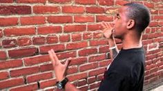 a man standing in front of a brick wall with his hand up to the side