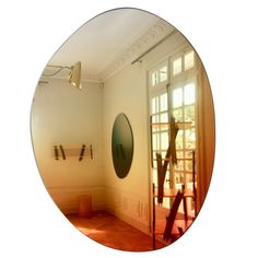 an oval mirror reflecting the inside of a room with wooden floors and white walls, in front of a doorway