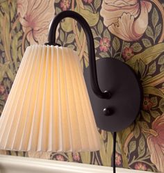 a lamp that is on the wall next to a flowered wall paper background with flowers