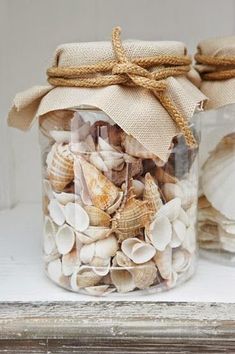 two glass jars filled with sea shells on top of a table