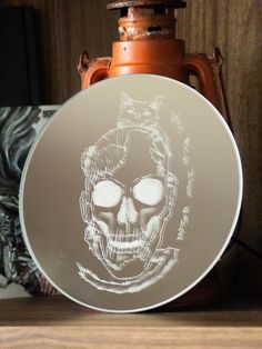 a glass plate with a drawing of a skull on it next to a brown vase