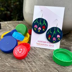 a pair of earrings sitting on top of a wooden table next to some plastic cups