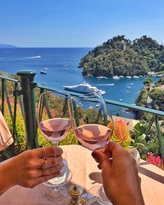 two people toasting wine glasses on a balcony overlooking the ocean