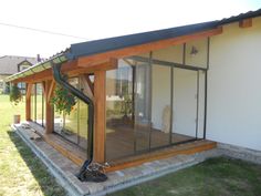 a small house with glass walls and wood trimmings on the roof, near a grassy area