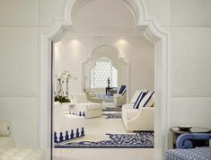 a living room filled with white furniture and blue rugs on the floor in front of a mirror