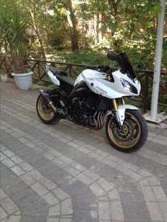 a white and black motorcycle parked on the side of a brick road next to trees