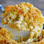 a spoon full of macaroni and cheese being lifted from a casserole dish