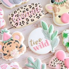 some decorated cookies are laying on a white wooden table with pink and green accents, including one that says wild