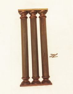 two antique brass pillars with nails on the bottom and one in the middle, against a white background