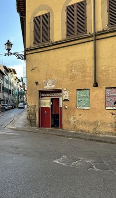 an old yellow building with shutters on the windows and a red door in front