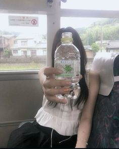 a woman sitting on a bus holding up a water bottle