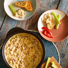 two plates with food on them next to some bread and celery sticks in bowls