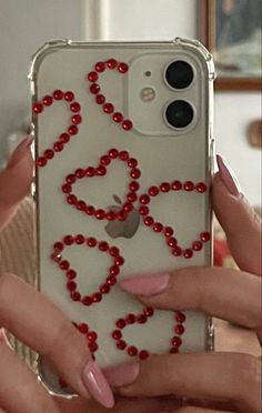 two hands holding an iphone case with red beads on it and hearts drawn on the back