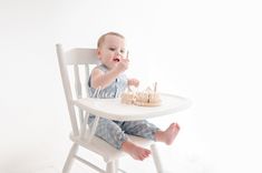 a baby sitting in a white high chair eating food from a toy house on the table