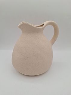 a white vase with a curved handle is on a table and it appears to be made out of clay