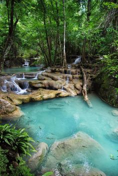 there is a blue pool in the middle of some rocks and trees with water running down it