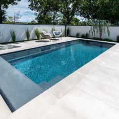 an empty swimming pool in the middle of a backyard with chairs and trees around it