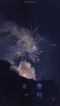 fireworks are lit up in the night sky above some building's roof tops and windows