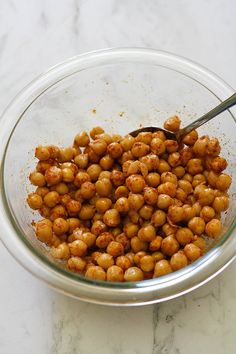 a glass bowl filled with chickpeas on top of a white counter next to a silver spoon