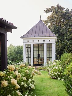 a gazebo in the middle of a garden with white flowers and greenery around it