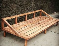 a wooden bench sitting on top of a cement floor next to a wall and sidewalk