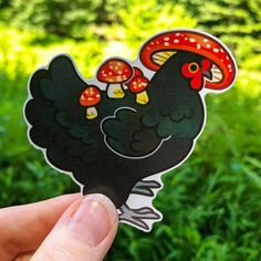 a hand holding up a sticker with a black rooster on it's head