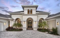 a large white house with lots of windows and palm trees in the front yard at dusk